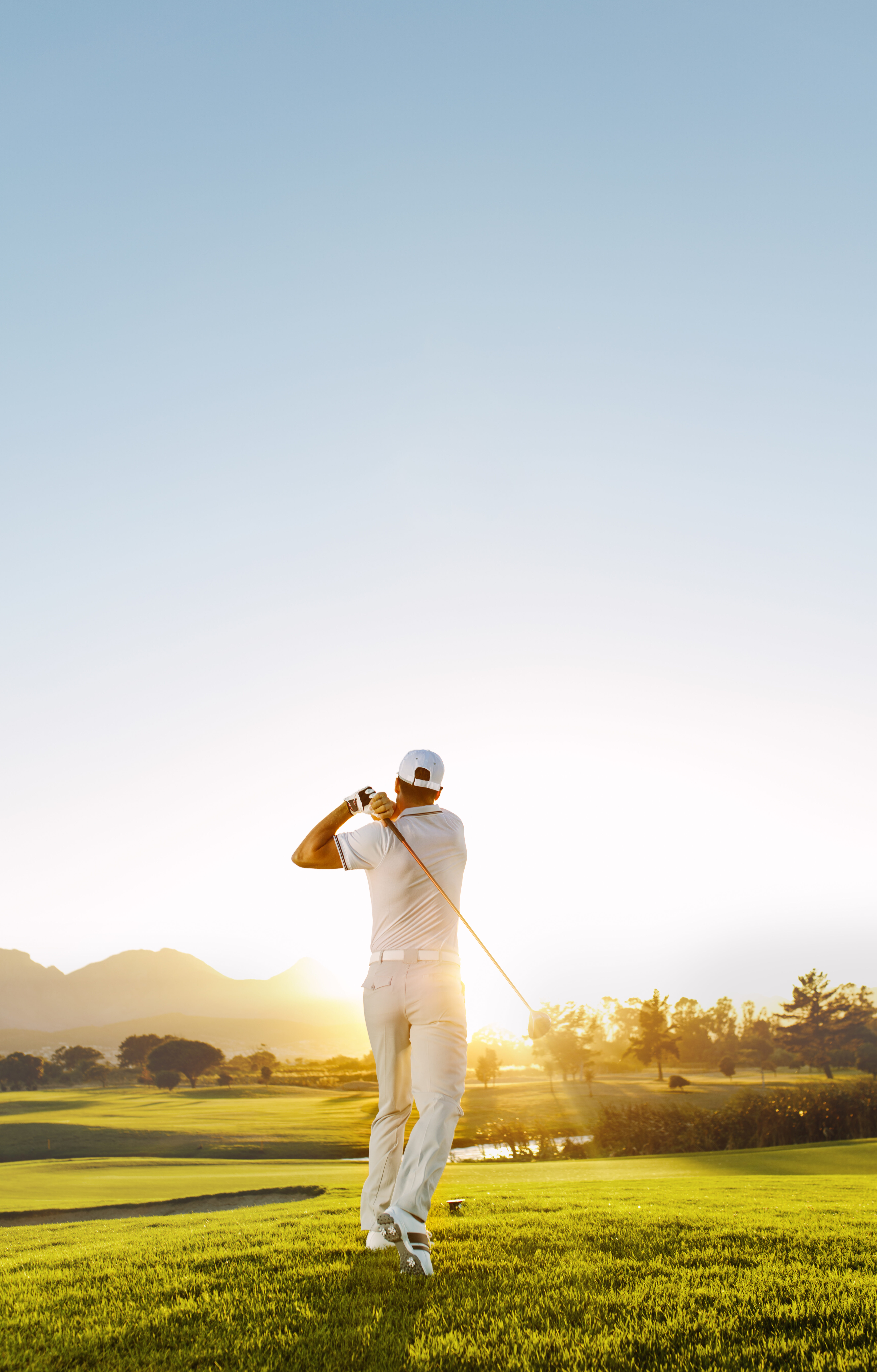 Rear view of golfer hitting driver on a golf course in the sun. Full length shot of young man playing golf on a sunny day.