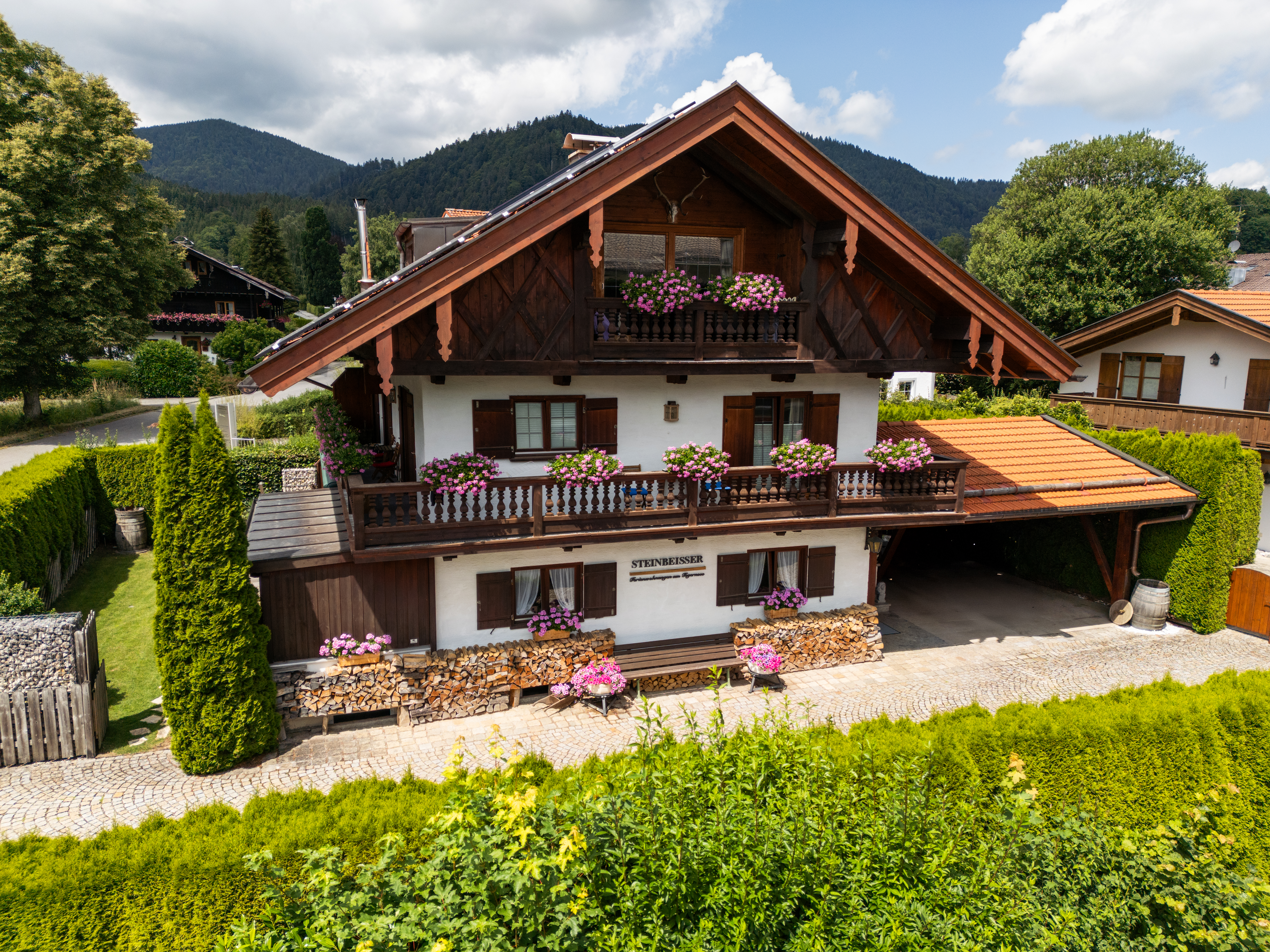 Hausansicht frontal eines traditionellen Hauses mit Holzvertäfelung vor Bergpanorama, gemütliche Ferienwohnungen in Bad Wiessee am Tgernsee