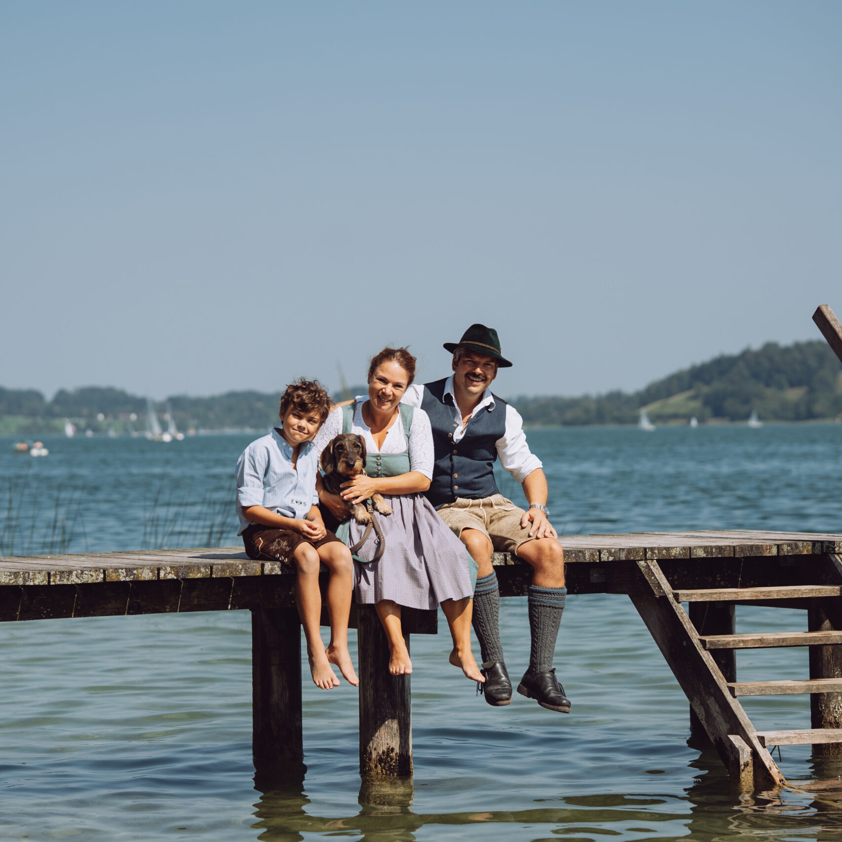 Familie Steinbeisser, Foto einer Familie mit einem Kind und Dackel auf einem Steg auf dem Tegernsee, Familie ist in traditioneller Tracht gekleidet